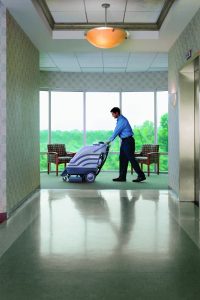 man walking with a carpet cleaning machine at the end of a hallway