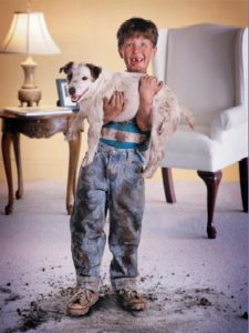 picture of a little boy with dirt all over him holding a dog with dirt on him standing inside on carpet with dirt all around